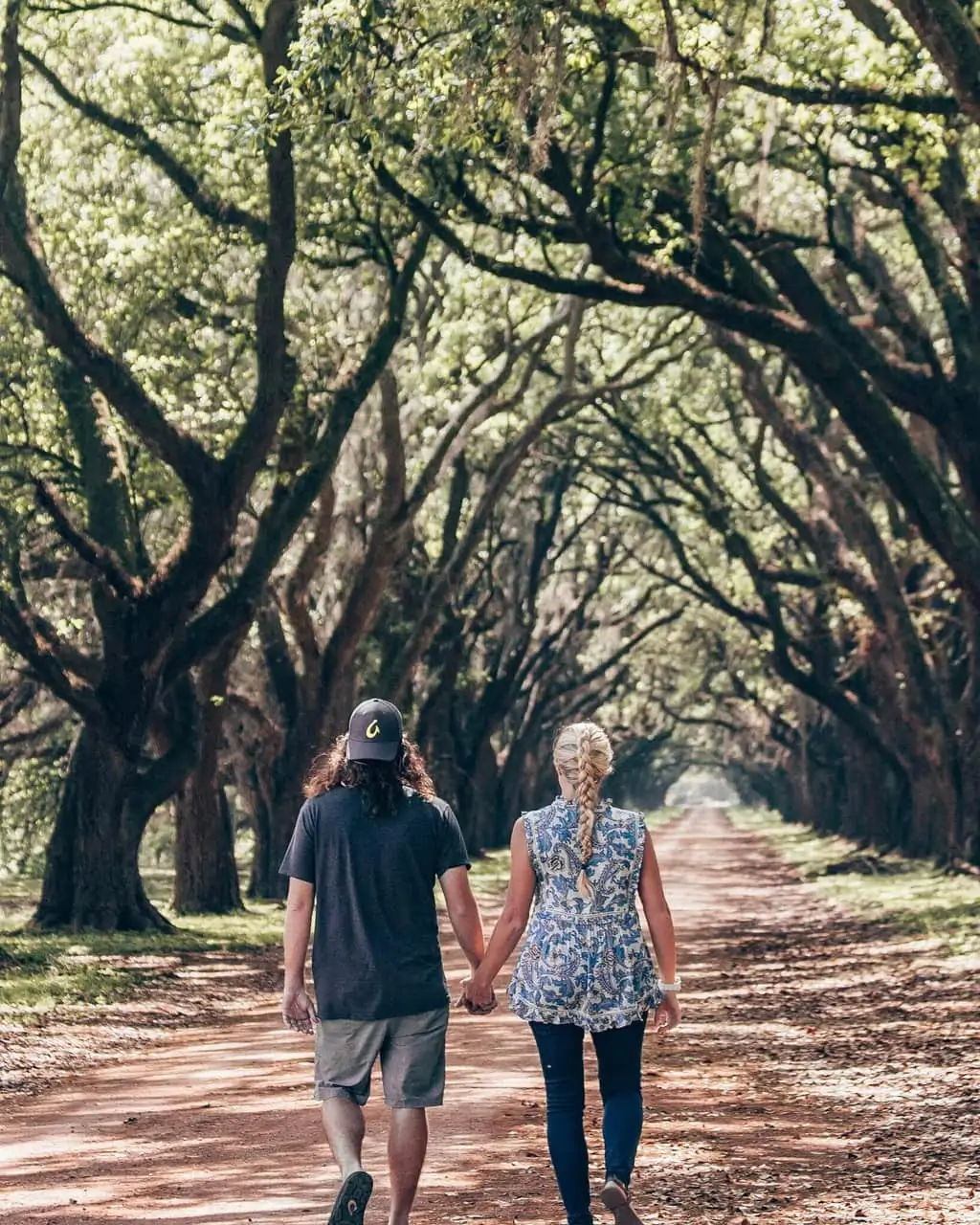 A couple holding hands and walking down an oak lined road in New Orleans at Evergreen Plantation