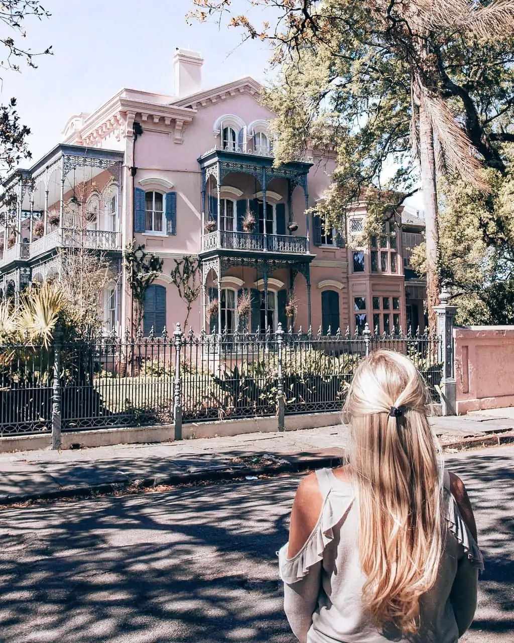 Blonde woman looking at a pink house in Garden District in New Orleans, Louisiana