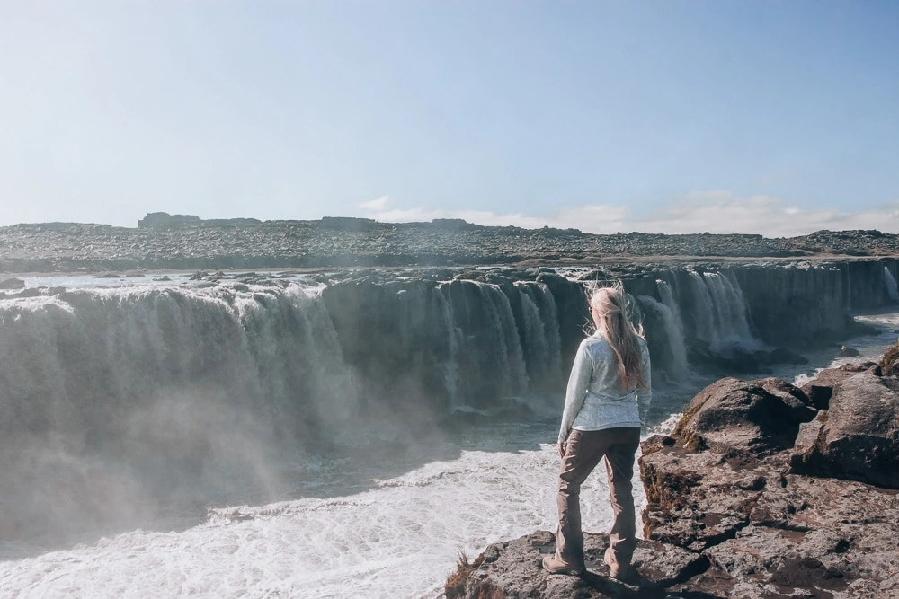 Standing on edge of cliff looking at Selfoss Waterfall in Iceland. Find the top 5 waterfalls in Iceland that you don't want to miss on a Ring Road road trip. 
