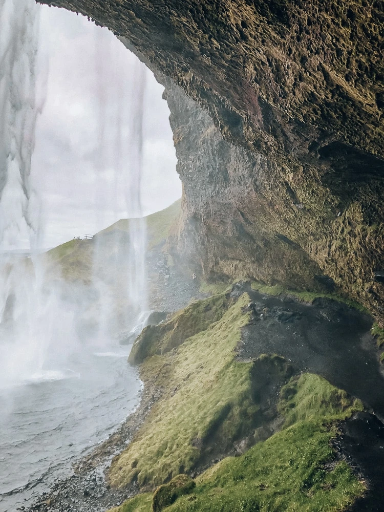 View from behind Seljalandsfoss waterfall in Iceland. Find the top 5 waterfalls in Iceland that you don't want to miss on a Ring Road road trip. 