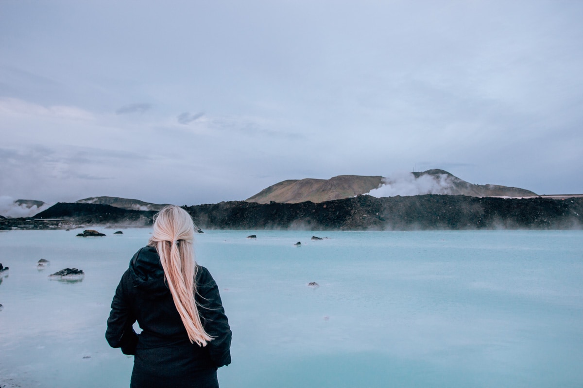 A woman standing by the Blue Lagoon Reykjavik in Iceland. Get a free guide to Iceland with a map to go with this full Ring Road itinerary.