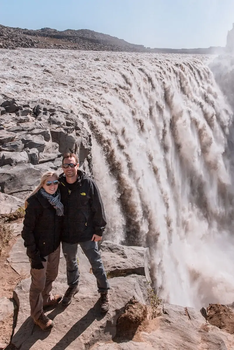 Couple standing by the edge of Dettifoss Waterfall in northern Iceland. Get a full Ring Road road trip guide with this 6 day Iceland itinerary.