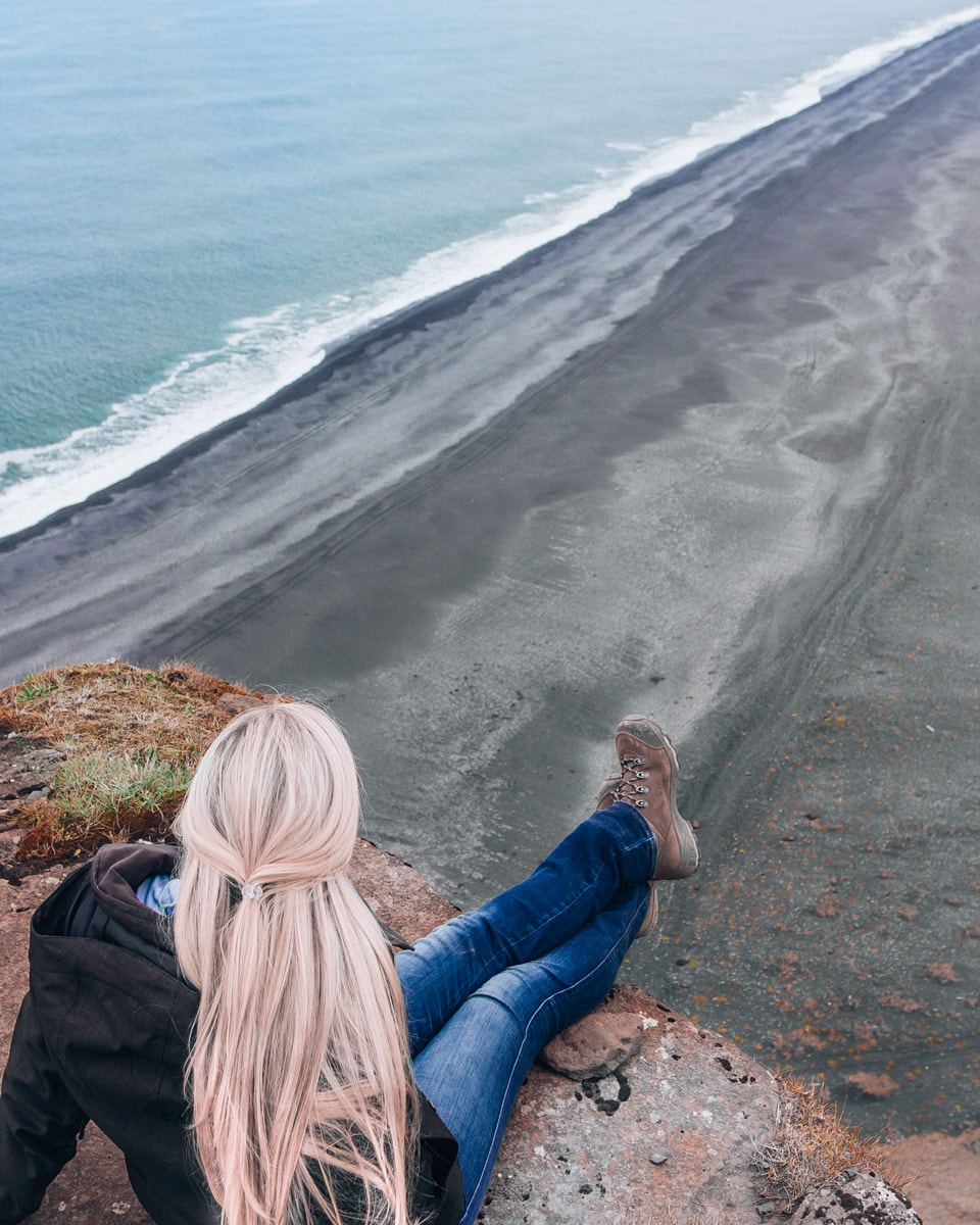 A woman overlooking the black sand beach from Dyrholaey in Iceland. All the best Iceland travel tips are in our Iceland travel guide and 6 day Iceland itinerary - click here for it!