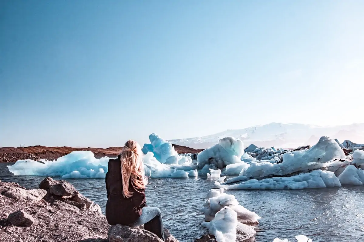Sitting on a rock on the edge of Iceland's glacier bay, Jokulsarlon. Get all the best stops for an Iceland road trip on our 6 day Iceland itinerary for Ring Road.