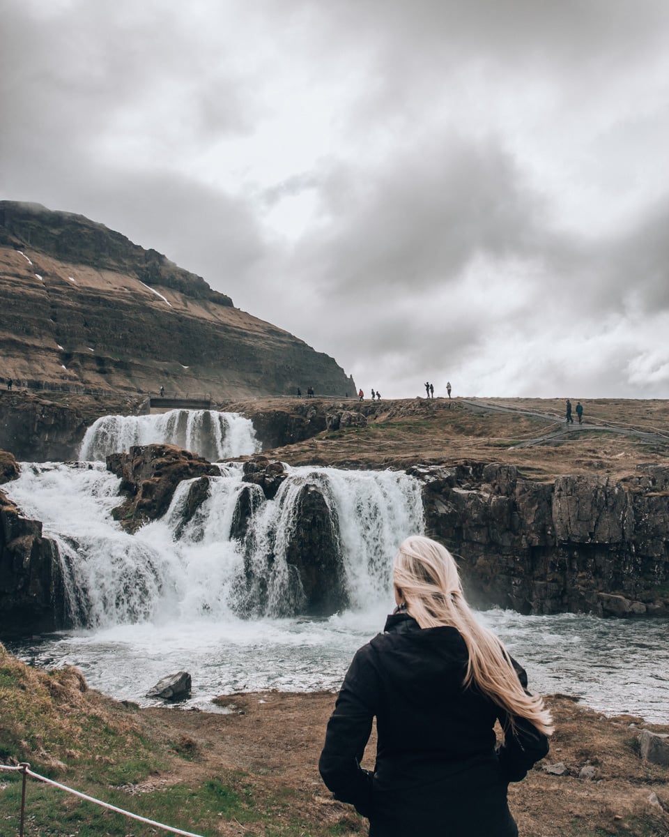 A woman looking at Kirkjufellsfoss in Iceland in the summer. Get the best stops for an Iceland road trip in summer with this full itinerary and map.