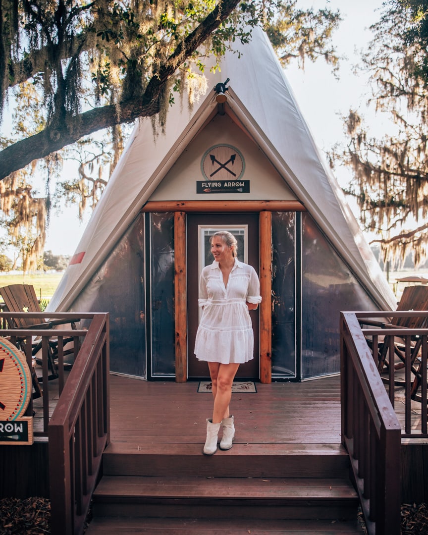 Woman in front of teepee in western inspired outfit with white dress and boots.