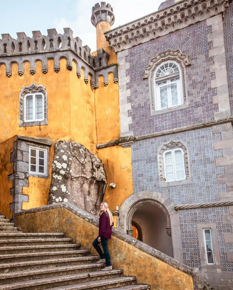A woman on the stairway in Pena Palace with different colors and textiles in the background.
