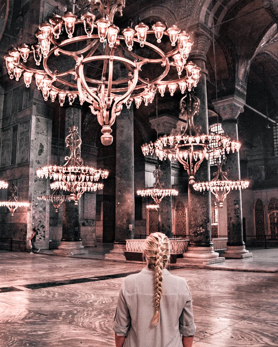 A woman inside of the Hagia Sophia in Istanbul admiring the chandeliers.