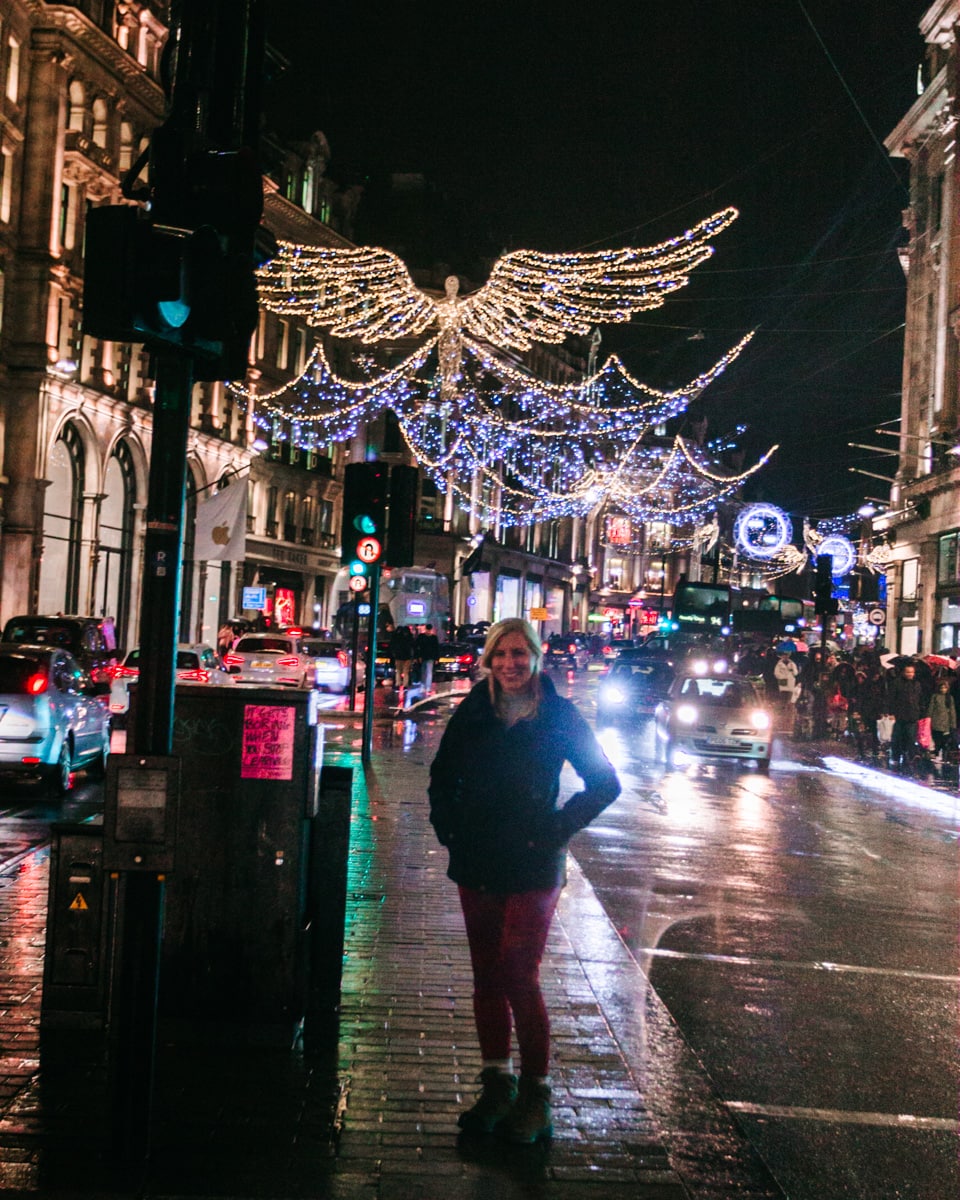 A woman standing in the median on Regent Street at Christmas with the angels twinkling above