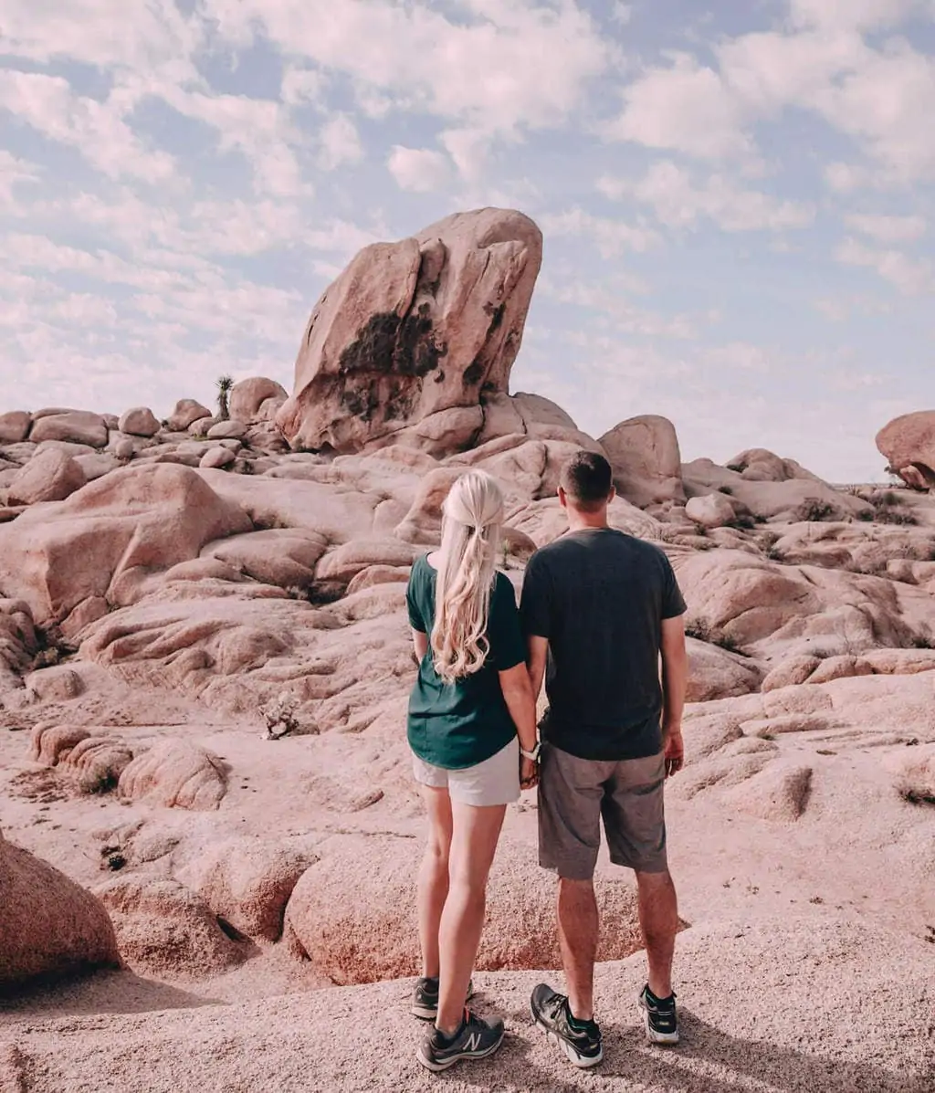 A couple holding hands and looking at the rock formations in Joshua Tree National Park near Arch Rock