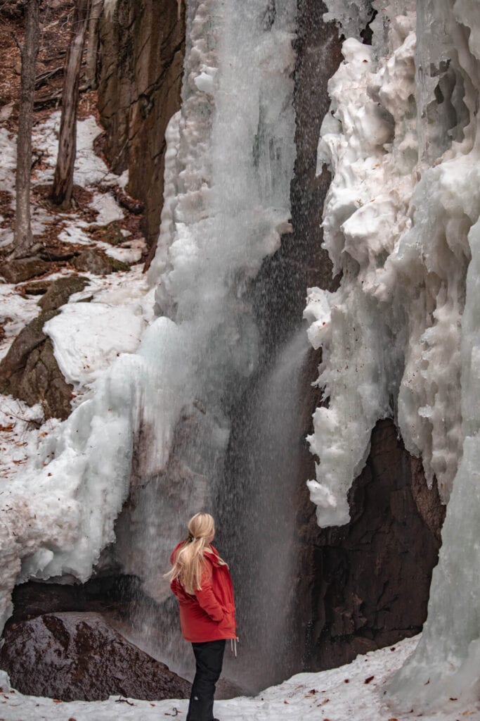woman standing beneath Champney Falls in winter
