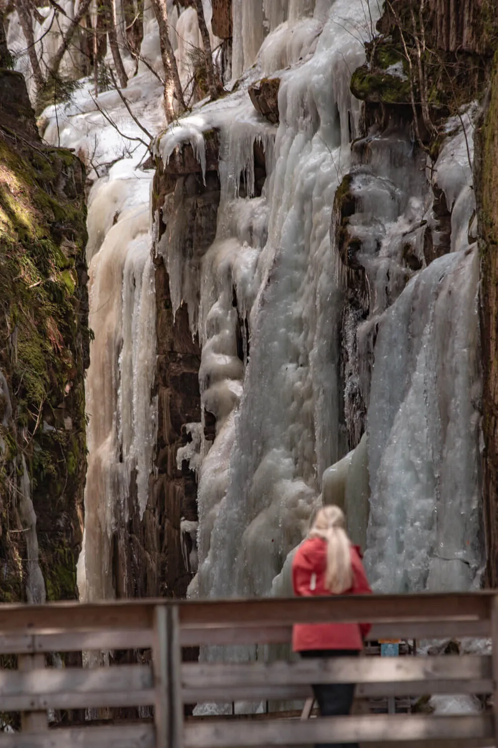 woman looking at frozen avalanche falls in franconia notch state park in winter