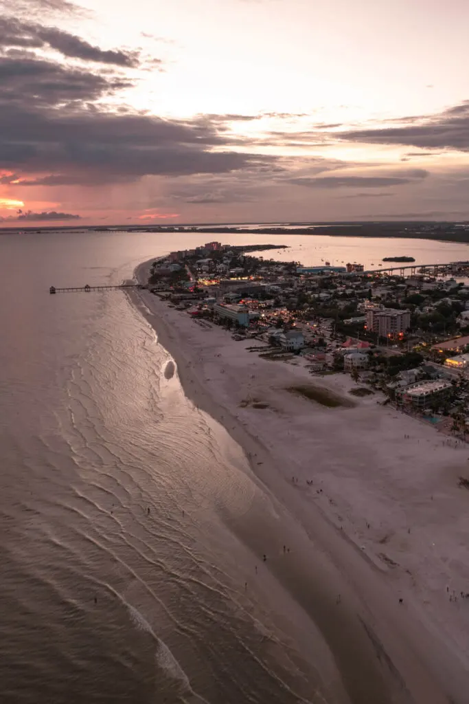 drone shot of sunset in fort myers beach with the pier,  matanzas pass bridge, and bowditch park