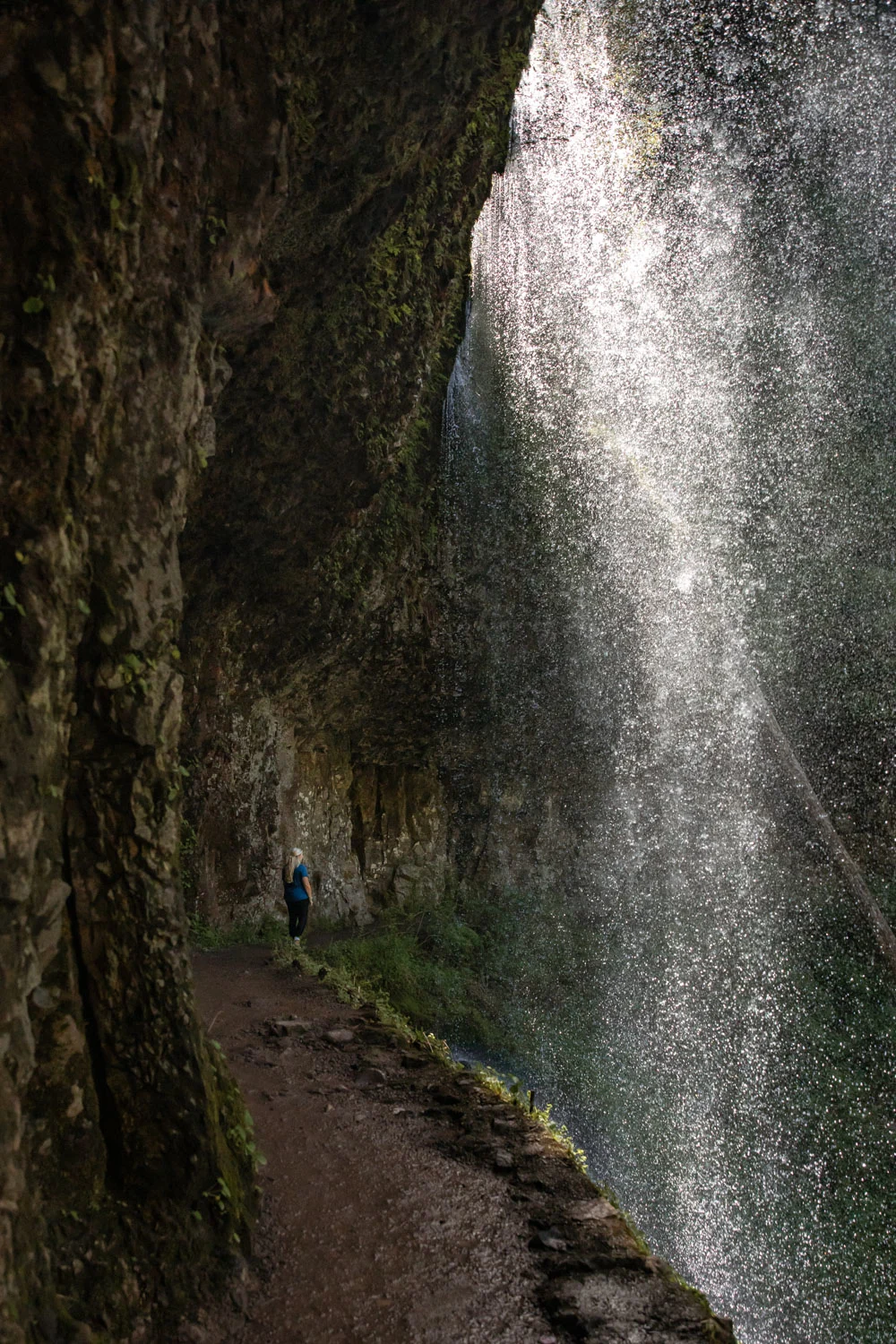 woman walking behind waterfall in Silver Falls State Park on the Trail of Ten Falls