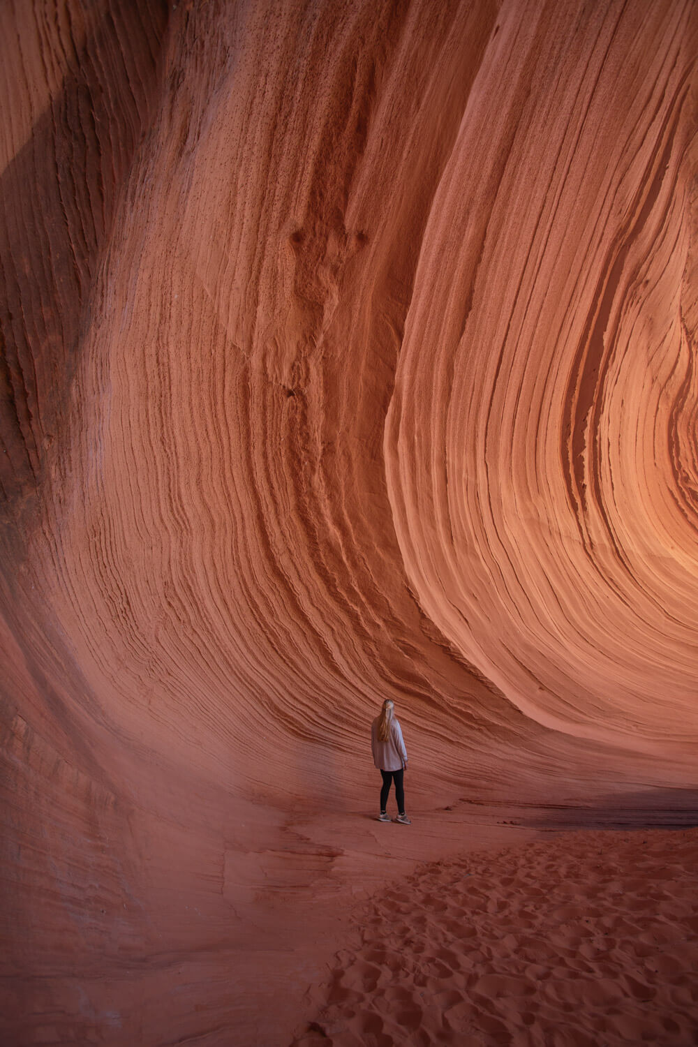 woman walking along the textured wall of the page sand cave
